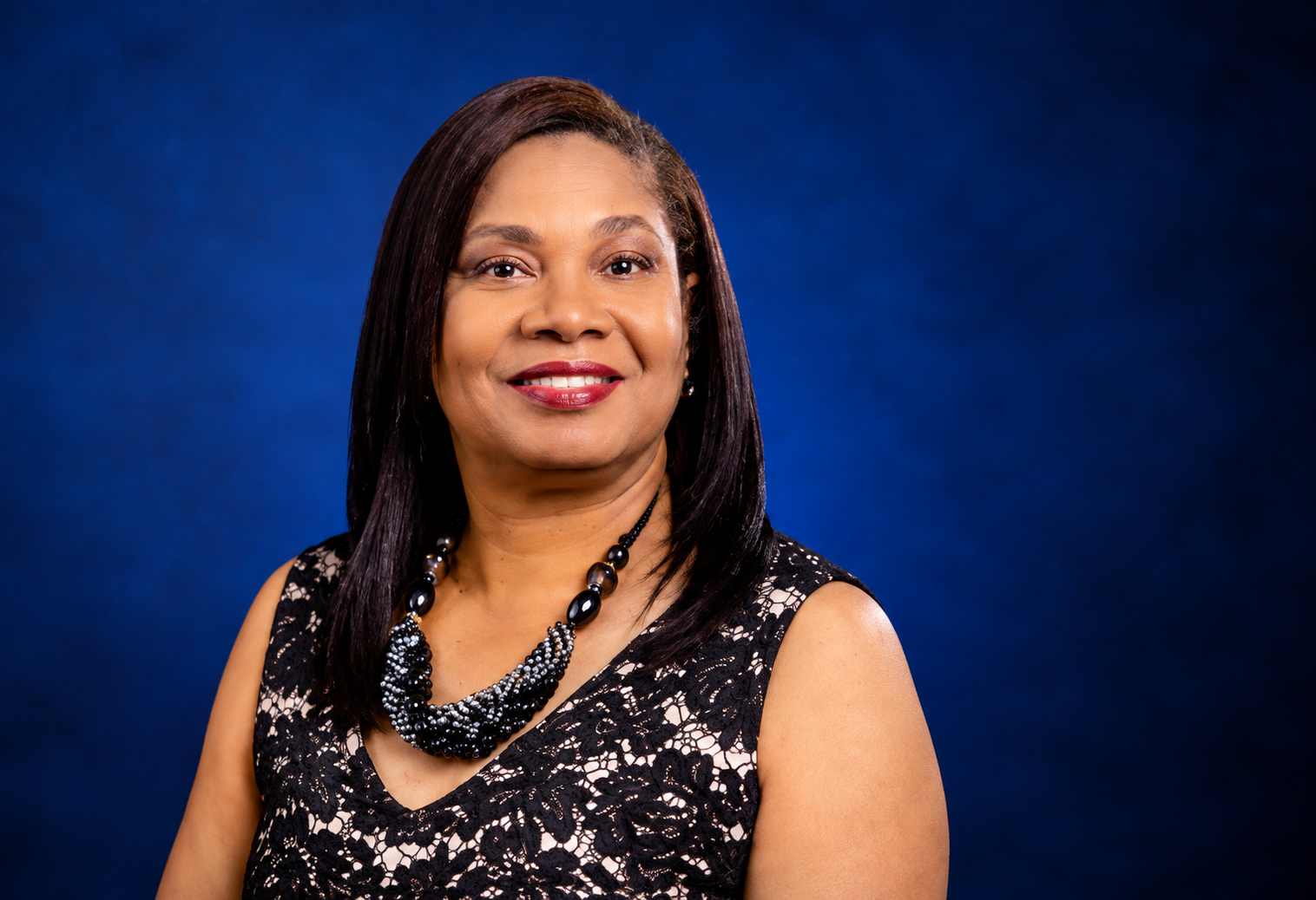The founder of Esthershouse, in a black lace dress with a beaded necklace, photographed against a deep navy backdrop